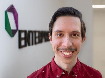 Ben Kass smiles at the camera while standing in front of the EK logo.